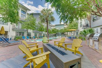 A sunny day at a poolside with yellow chairs and a fire pit.